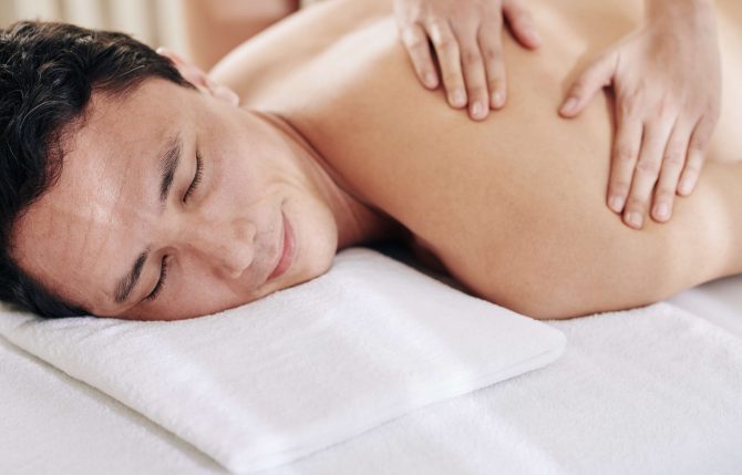 Good-looking smiling man enjoying deep tissue back and shoulder massage in spa salon
