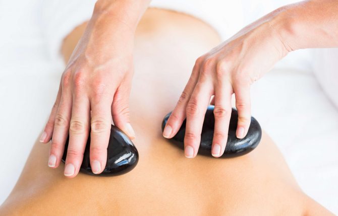 Cropped image of masseur giving hot stone massage on woman back at spa