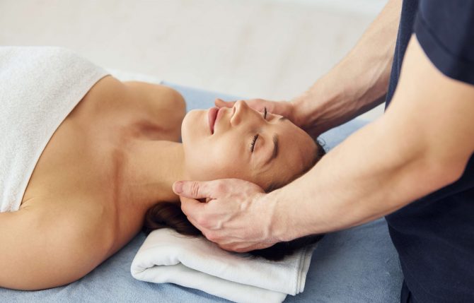 Head massage. Young woman is lying down when man doing procedure to her in spa.