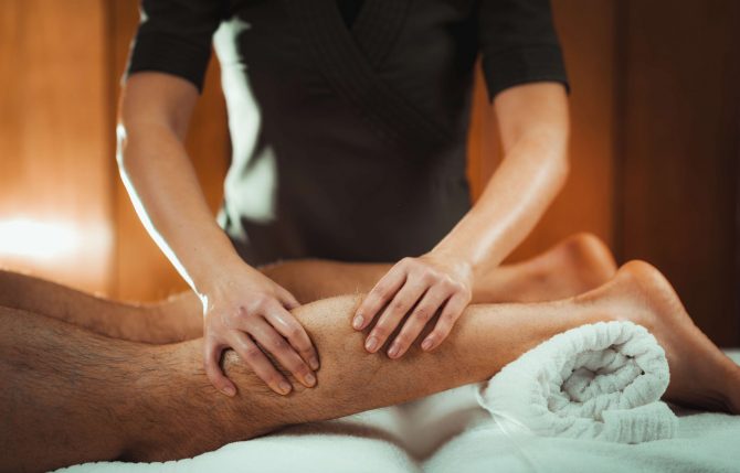 Physiotherapist massaging male patient with injured leg - calf muscle. Sports injury treatment.